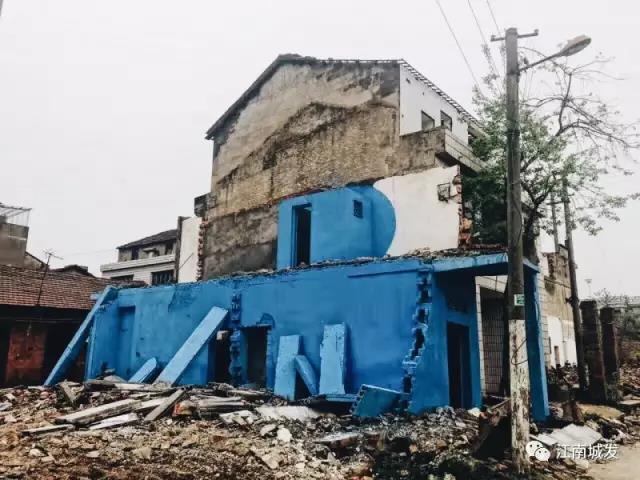 △ 這棟建筑是臨江最近的半拆遷建筑物的遺留，沅江和堤壩成為了展覽的天然背景。創(chuàng)作團(tuán)隊對這棟建筑進(jìn)行了半涂裝，將符號性的沅水曲線與拆遷進(jìn)行中的建筑立面進(jìn)行意義的疊造，它們共同觸發(fā)了場所空間多元語境的生成，把拆遷這種暫時破壞性、干擾性的介入行動與沅水右岸發(fā)展的未來性、美好性緊密融合。